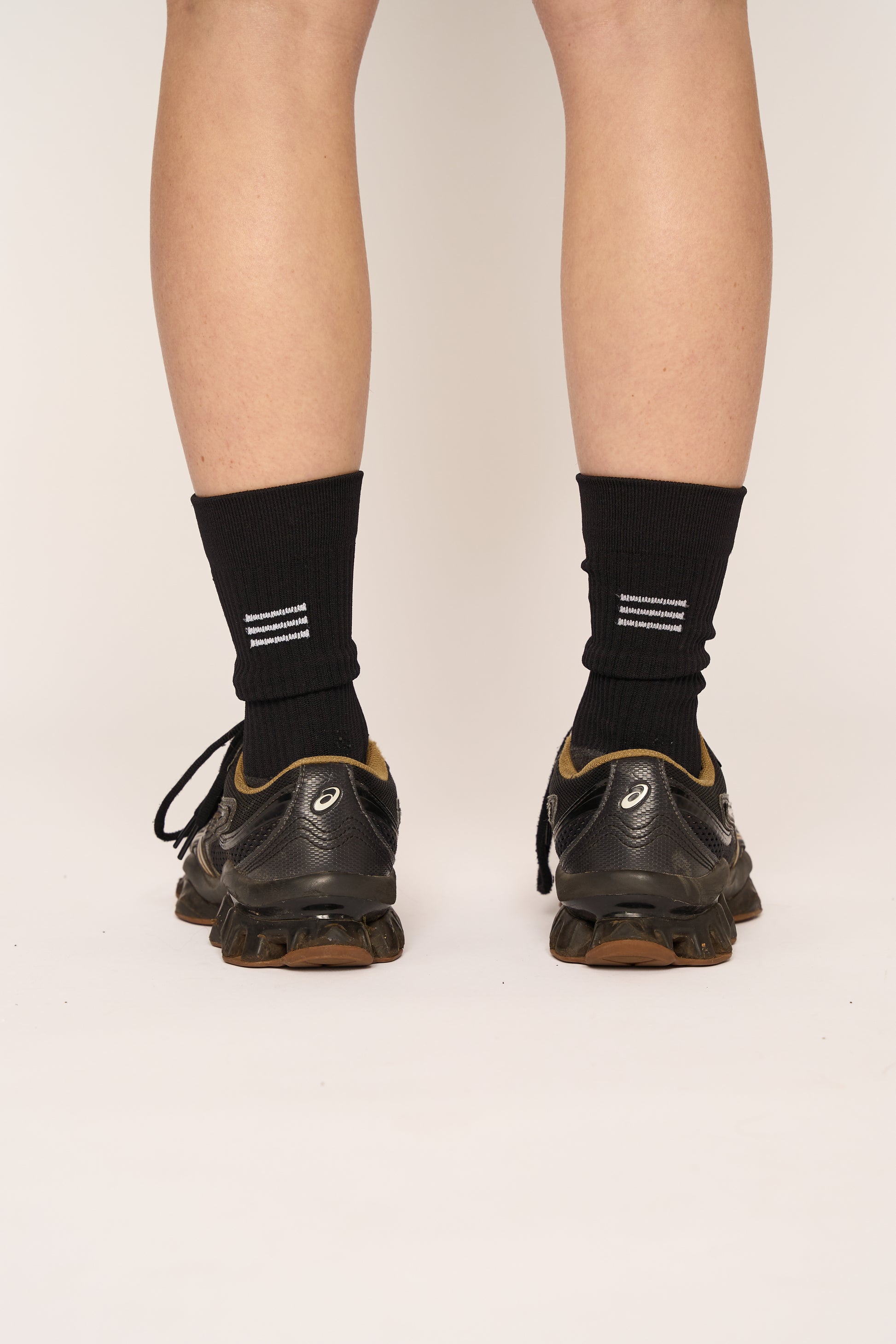 THE DELIVERY SOCKS in black, featuring a sporty design, worn with athletic shoes from a rear view.