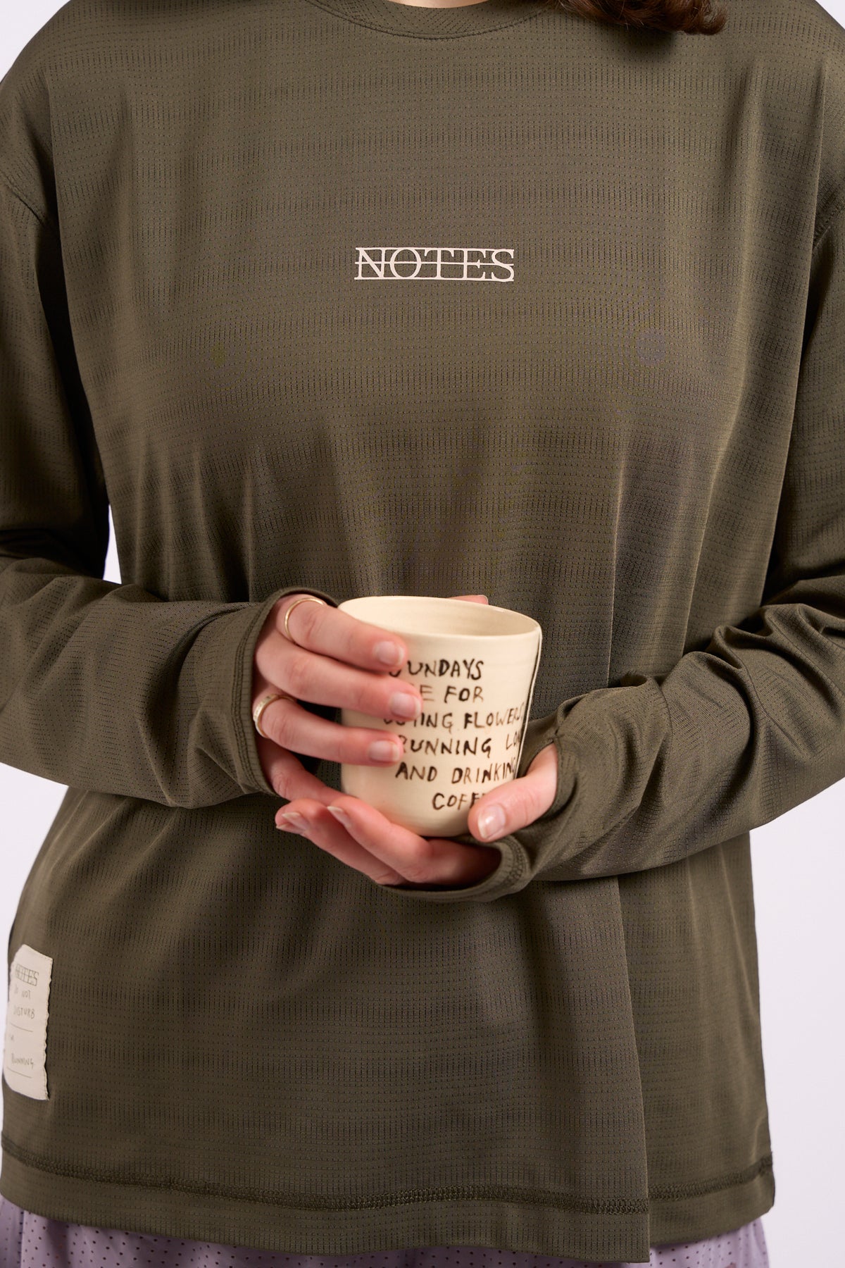 Long Note LS Performance Tee in olive, on model holding a cup, front detail