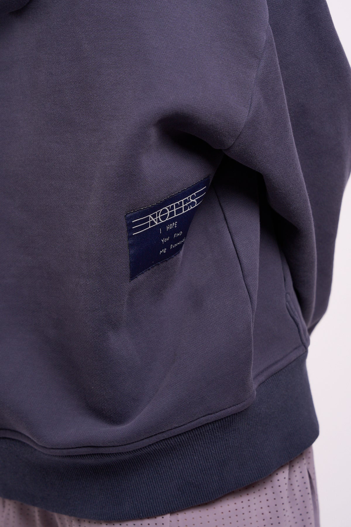 Warm Down Hoodie in Washed Pelagic Blue, close-up of Notes label at hem