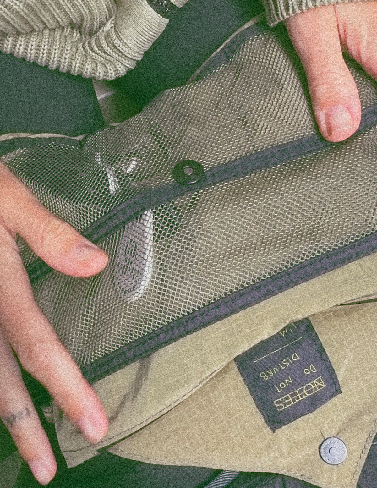Musette Messenger Running Bag in Olive/Black, close-up of front mesh pocket and Notes label