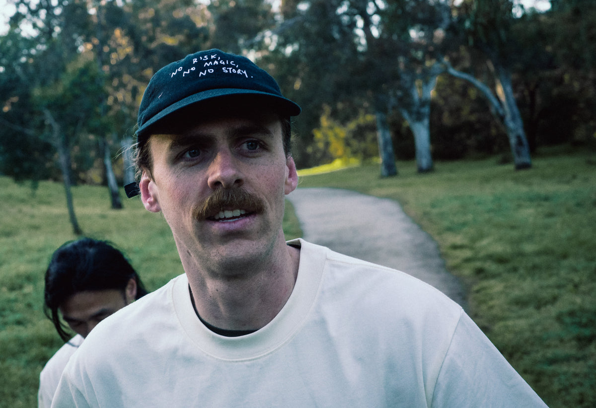 Runner wearing the No Risk No Magic No Story Cap in Washed Black on a grassy trail