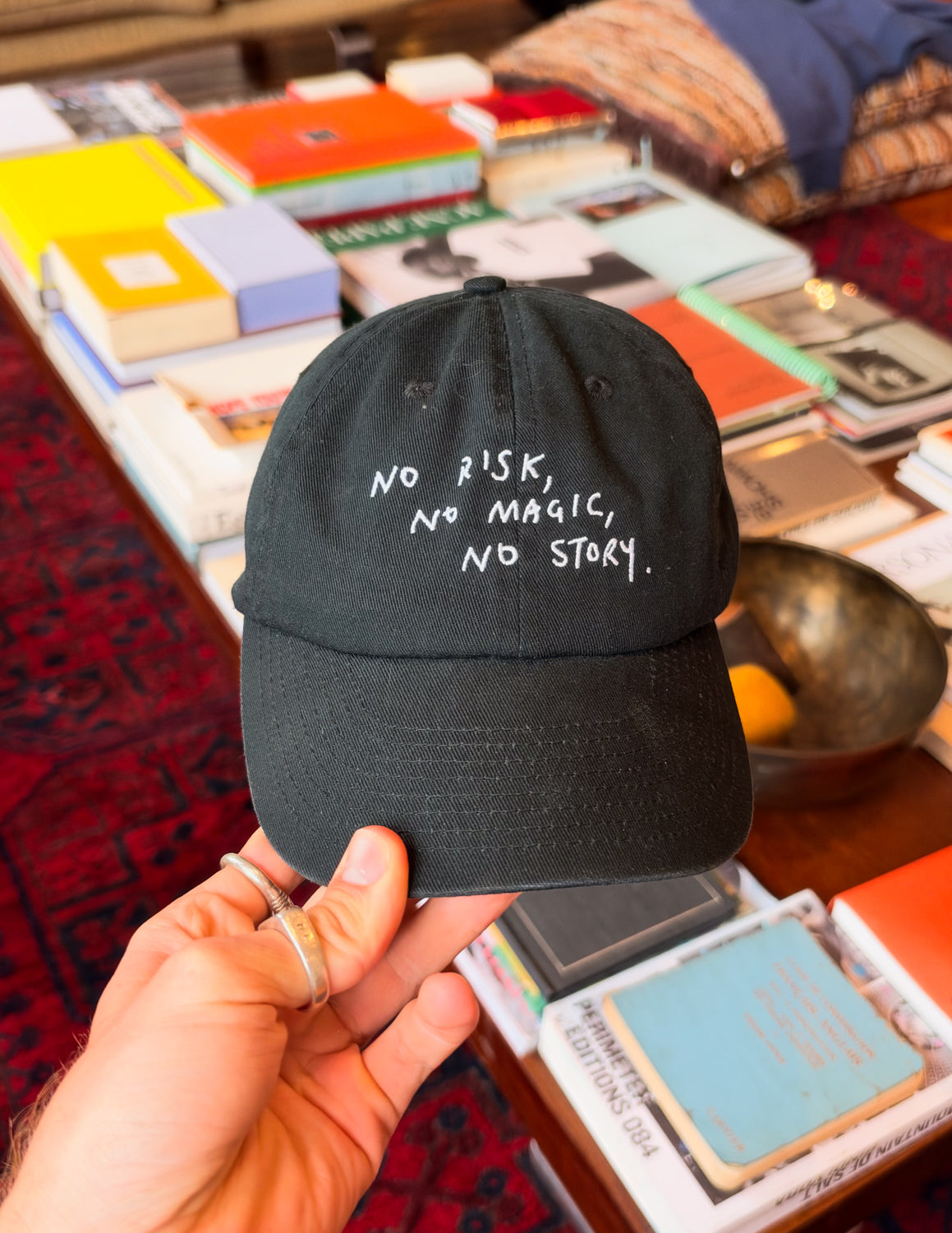 No Risk No Magic No Story Cap in Washed Black held in hand, front text "No Risk, No Magic, No Story"